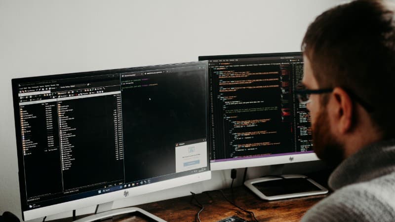 Software developer typing code on dual monitors at a wooden desk., tags: casino california's drop - pexel