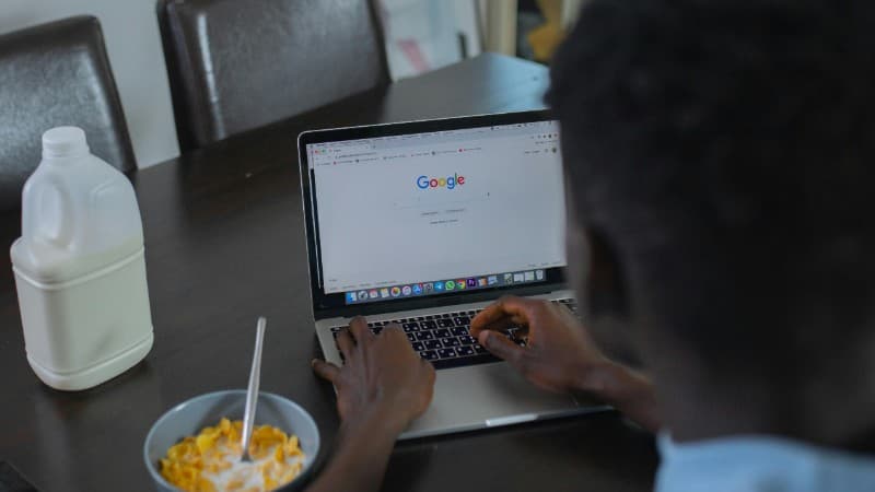 A person browsing Google on a laptop while having cereal breakfast at the table. - A person browsing Google on a laptop while having cereal breakfast at the table., tags: gambling - pexel