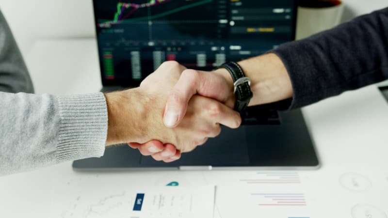 Close-up of a handshake with financial graphs on laptop screen, symbolizing a successful agreement., tags: casino affiliate network - pexel