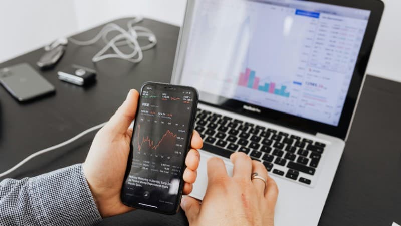 Person analyzes stock data with a smartphone and laptop, indoors., tags: casino affiliate - pexel