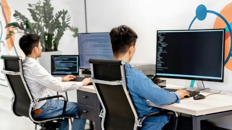 Two male developers at desks programming in a modern office workspace with large monitors., tags: hosting casino affiliate - pexel